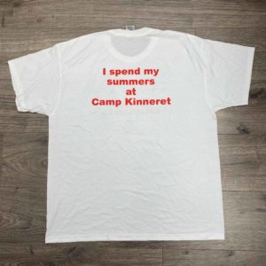 White T-shirt on a wooden floor displaying red text: "I spend my summers at Camp Kinneret.